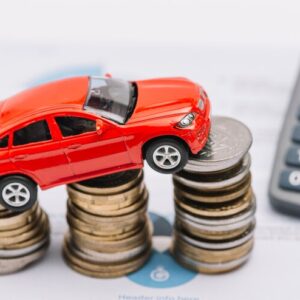 A person using a car loan EMI calculator on a laptop with a car model and financial charts in the background.